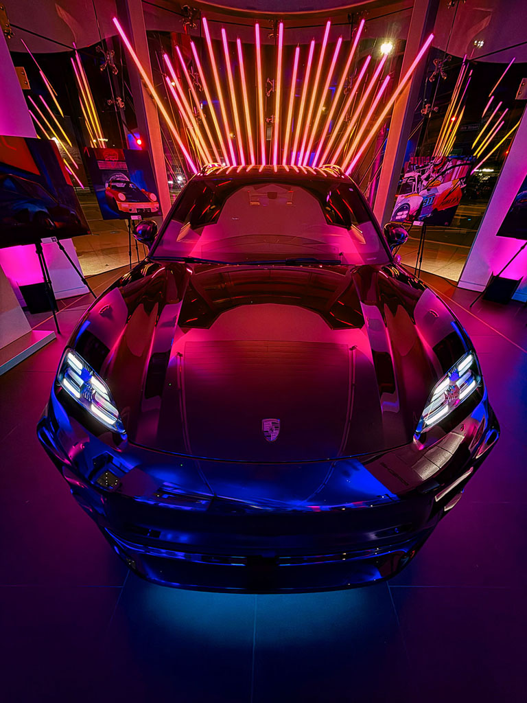 Front view of the Porsche Macan Electric beneath a fan of warm LED tubes.