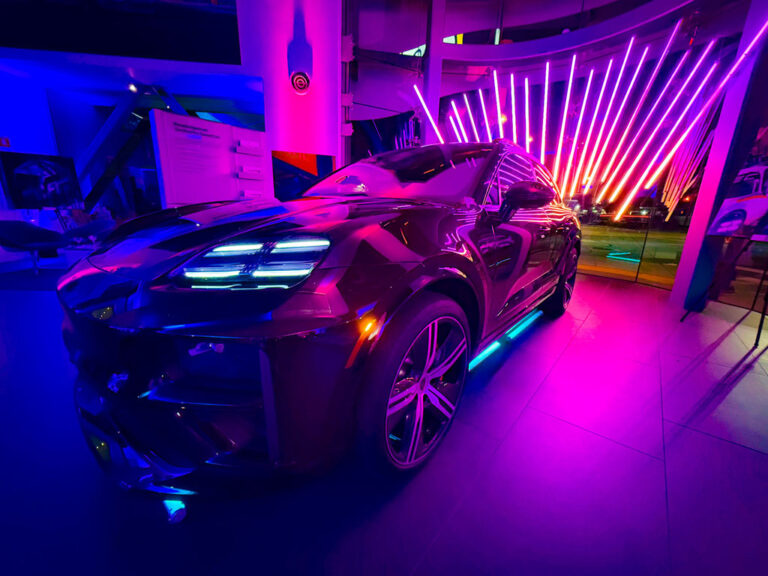 Porsche Macan Electric in a showroom filled with purple lighting and diagonal LED tubes.