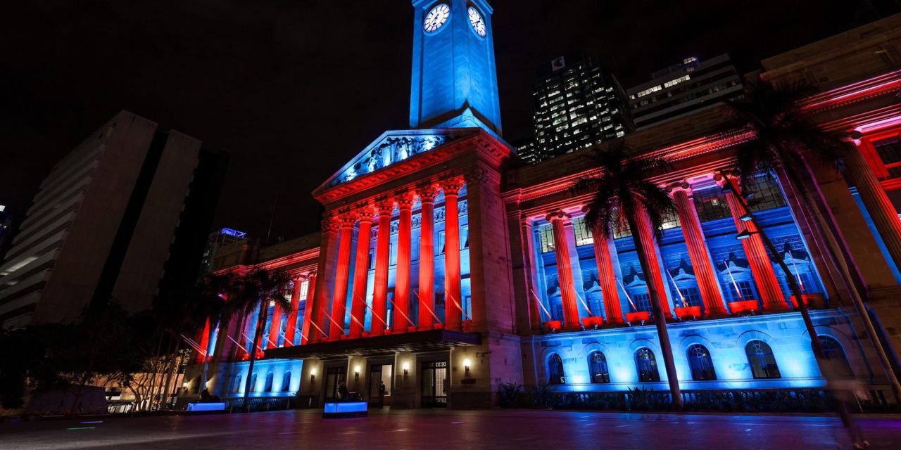 Brisbane City Hall illuminated in red and blue at night.