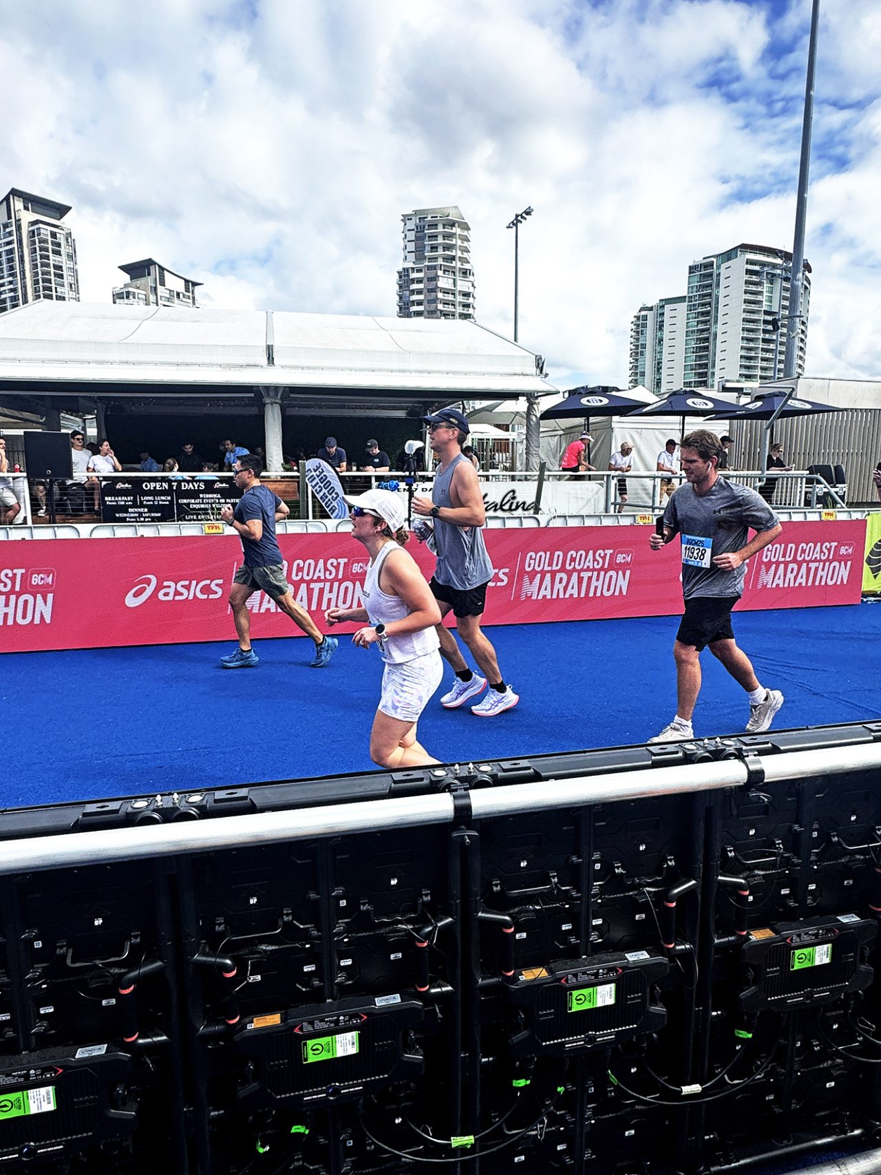 Runners passing blue finish-line flooring beside LED displays at the 2025 Gold Coast Marathon.