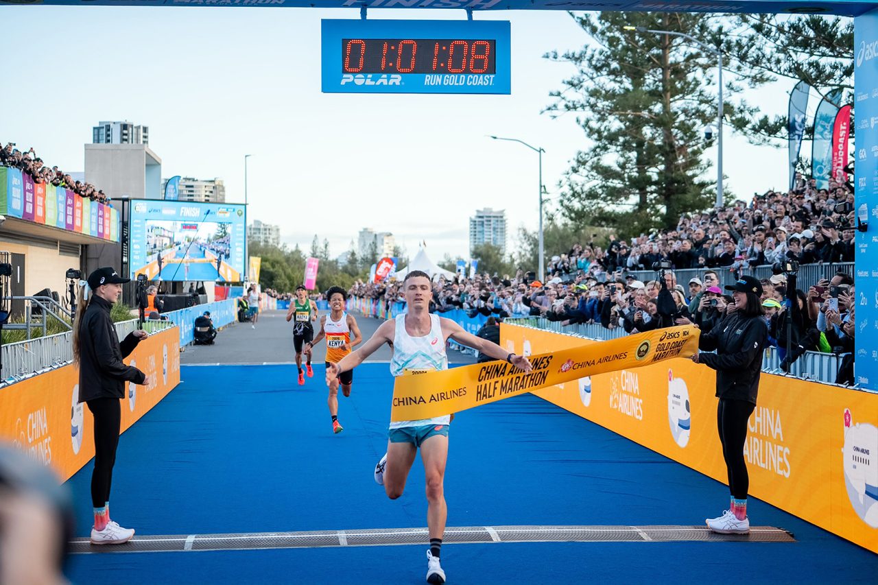 Runner breaking a yellow finish tape beneath the race clock at the Gold Coast Marathon.