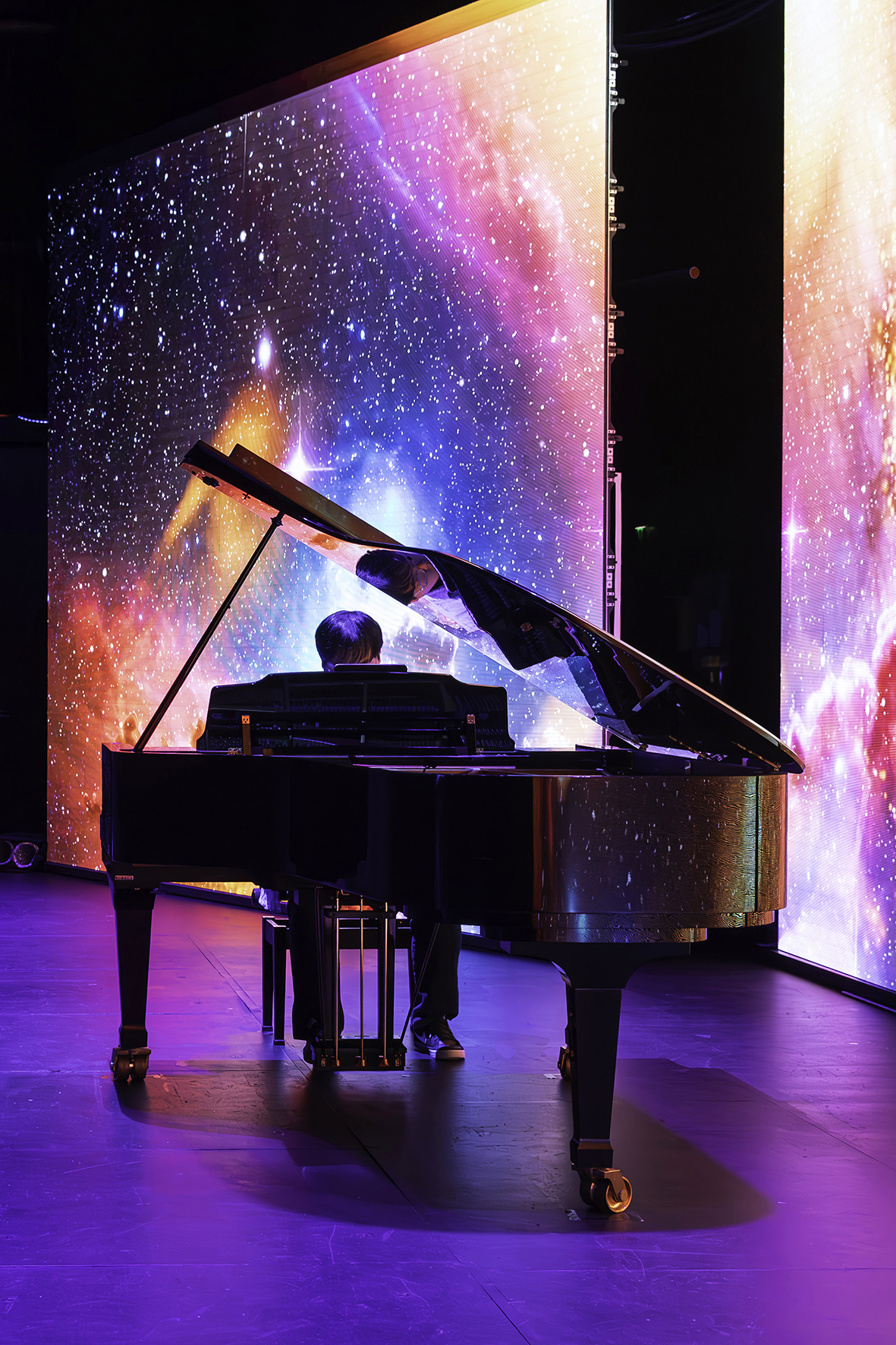 Pianist at a grand piano in front of a colourful vertical LED screen at TAUMATA 2025.