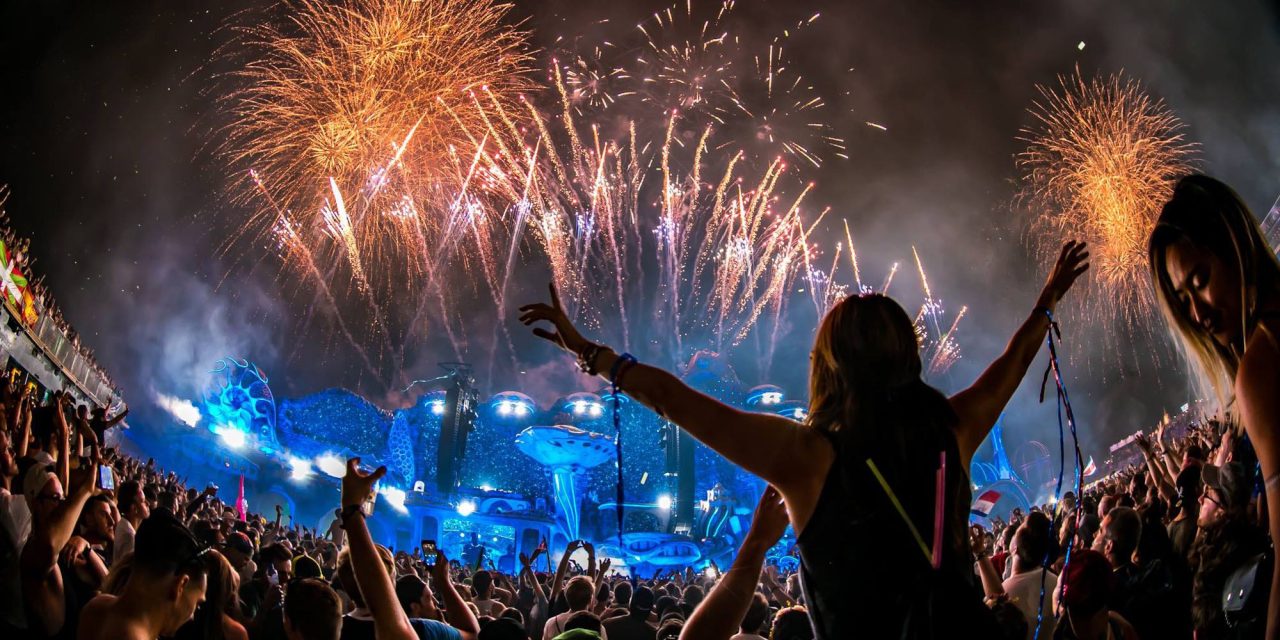 Festivalgoer raising both arms as fireworks burst above the Tomorrowland crowd.