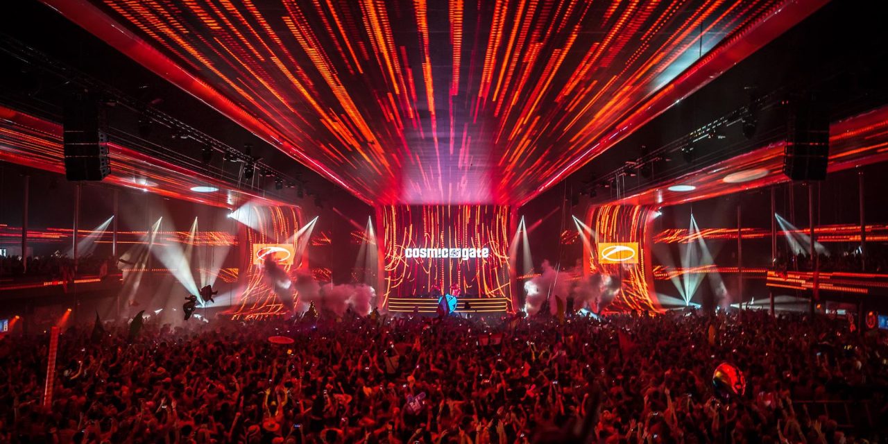 Red beams spreading over a packed indoor Tomorrowland stage and audience.