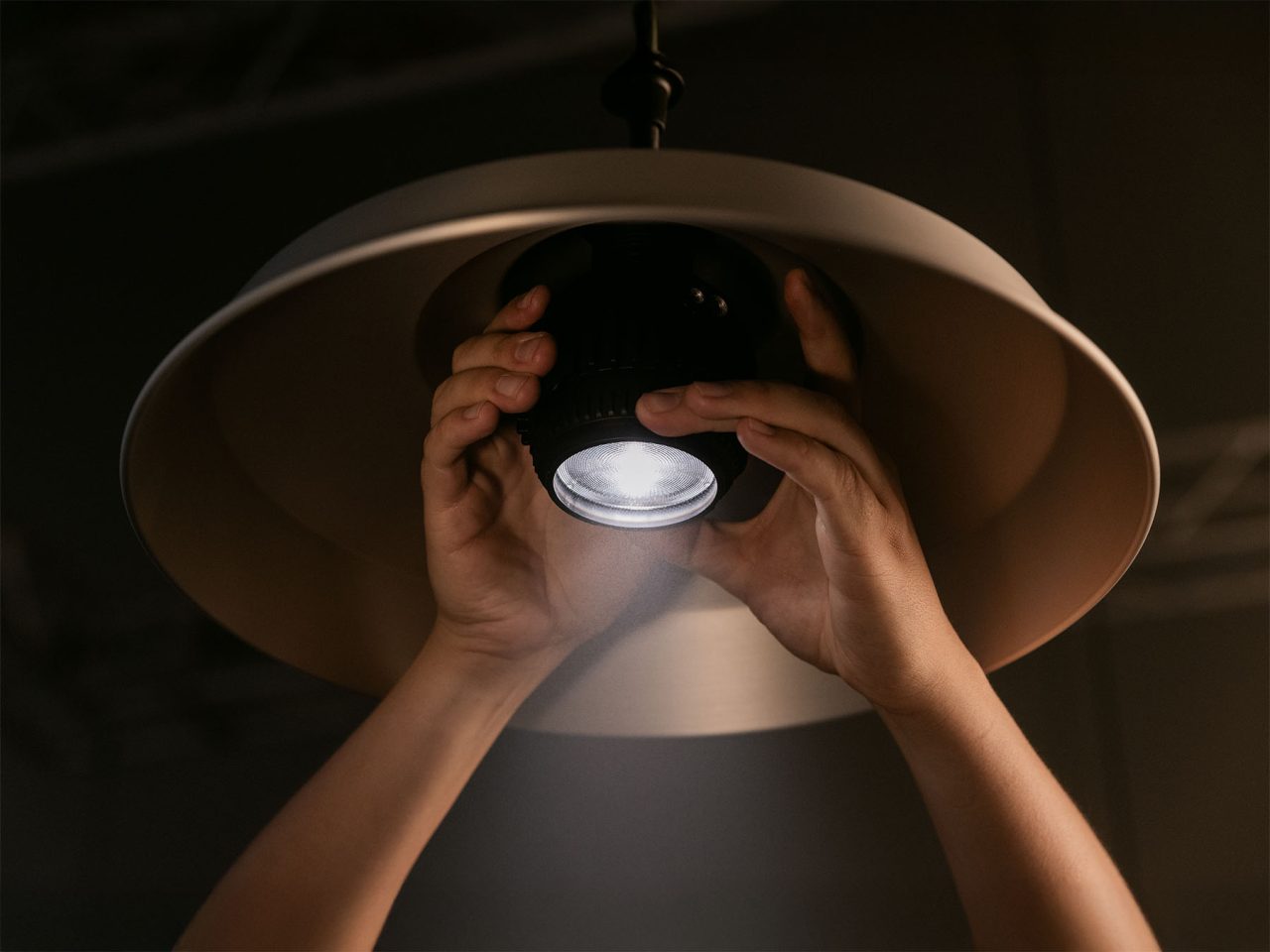 Hands fitting an Astera SolaBulb beneath a large lampshade.