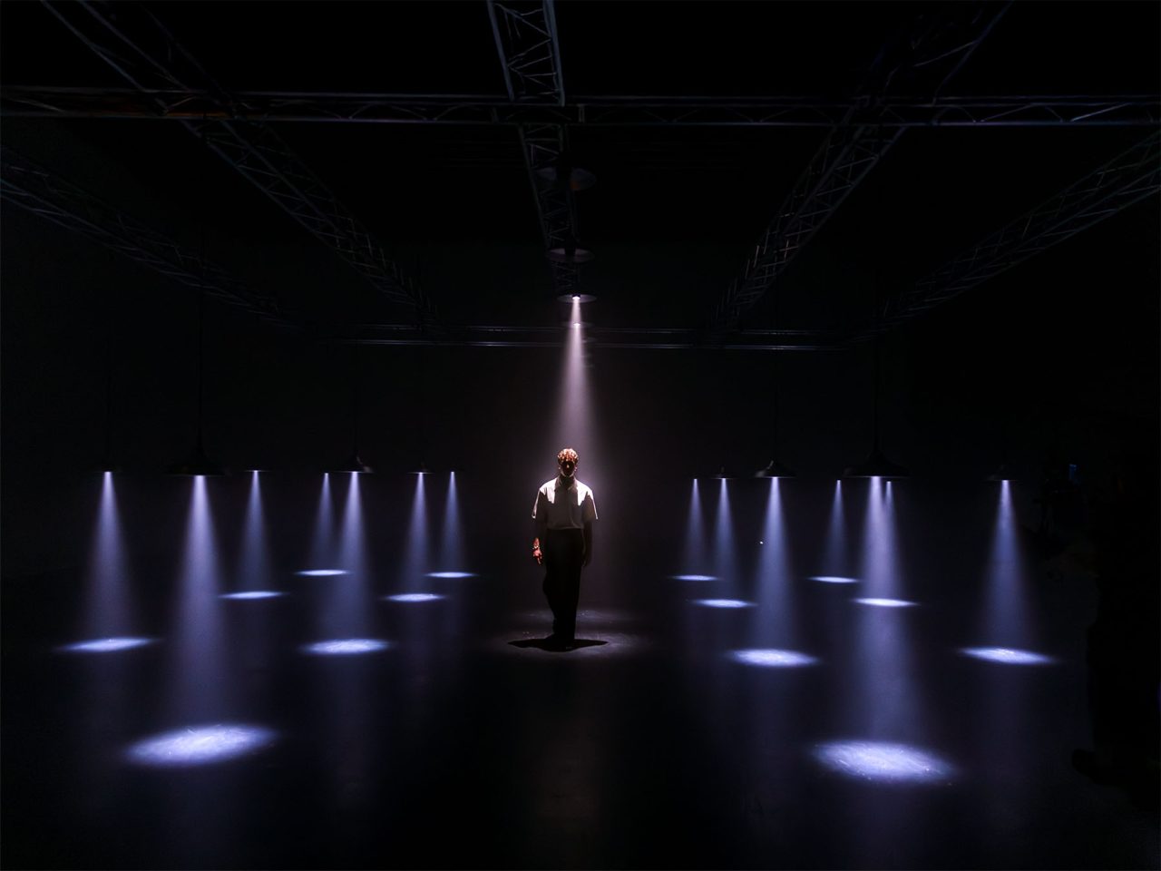 Rows of narrow white spotlights forming pools of light around a performer.