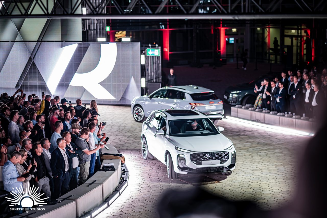 Two Audi Q3 vehicles driving past guests at the launch event.