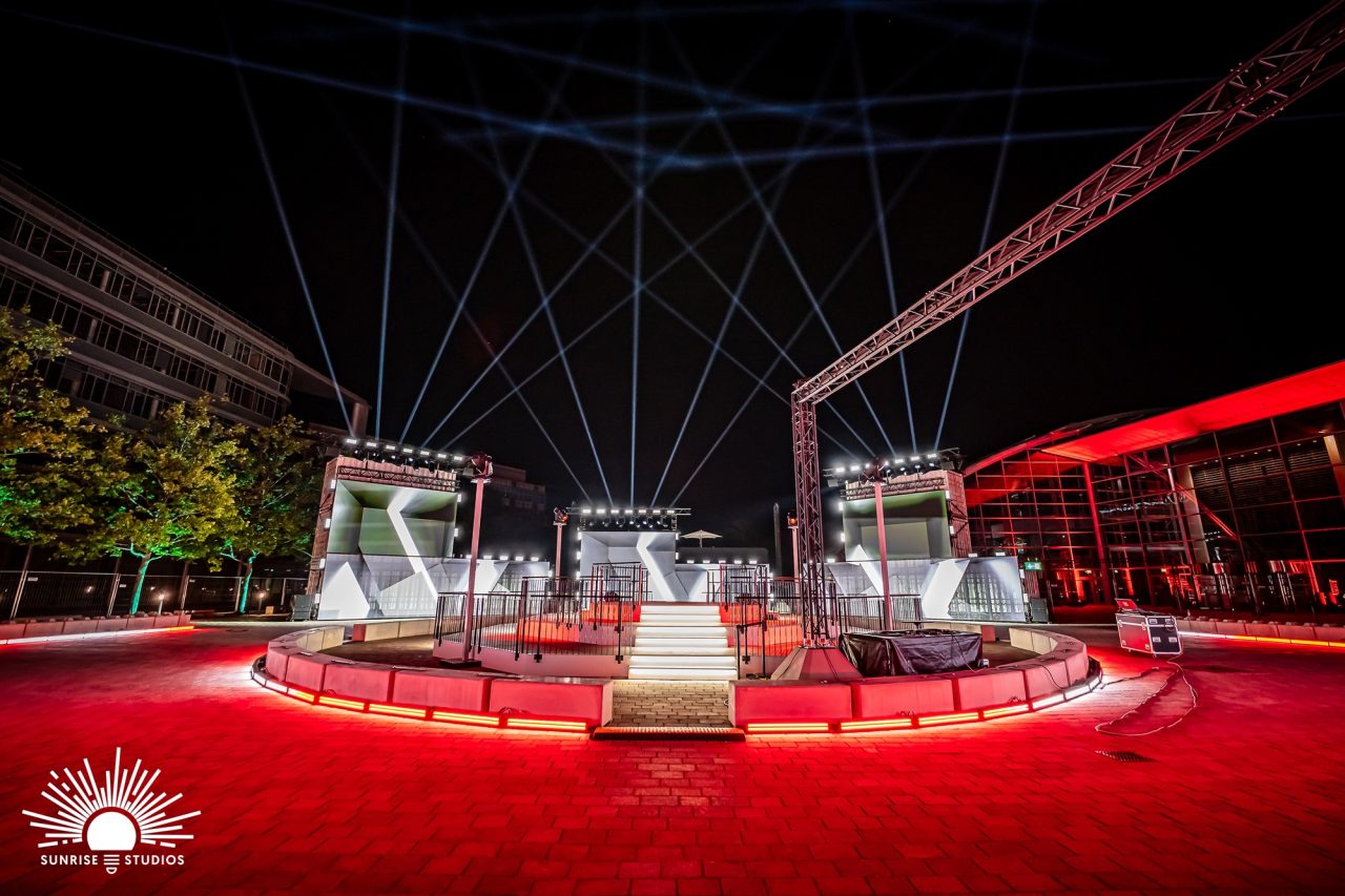 Wide view of the Audi Q3 launch venue with a red circular stage and overhead beams.