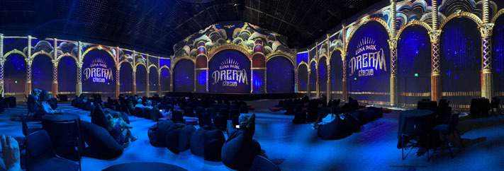 Visitors seated in an immersive gallery with blue and gold projections across arched walls.