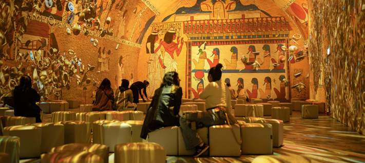 Visitors exploring an immersive room filled with Egyptian-inspired wall projections.