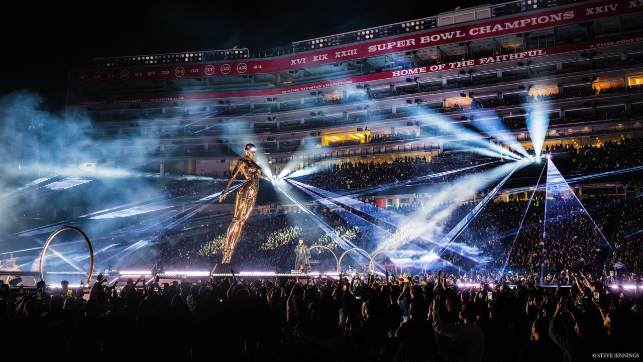 White beams radiating across The Weeknd's stadium stage and audience.