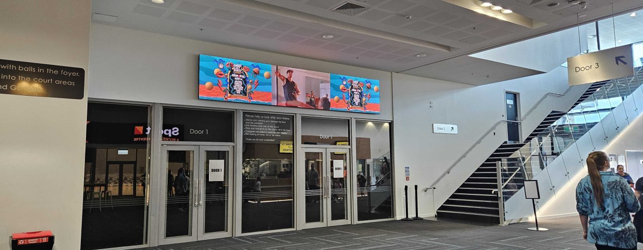 Wide LED display above the interior entry doors at Baypark Arena.