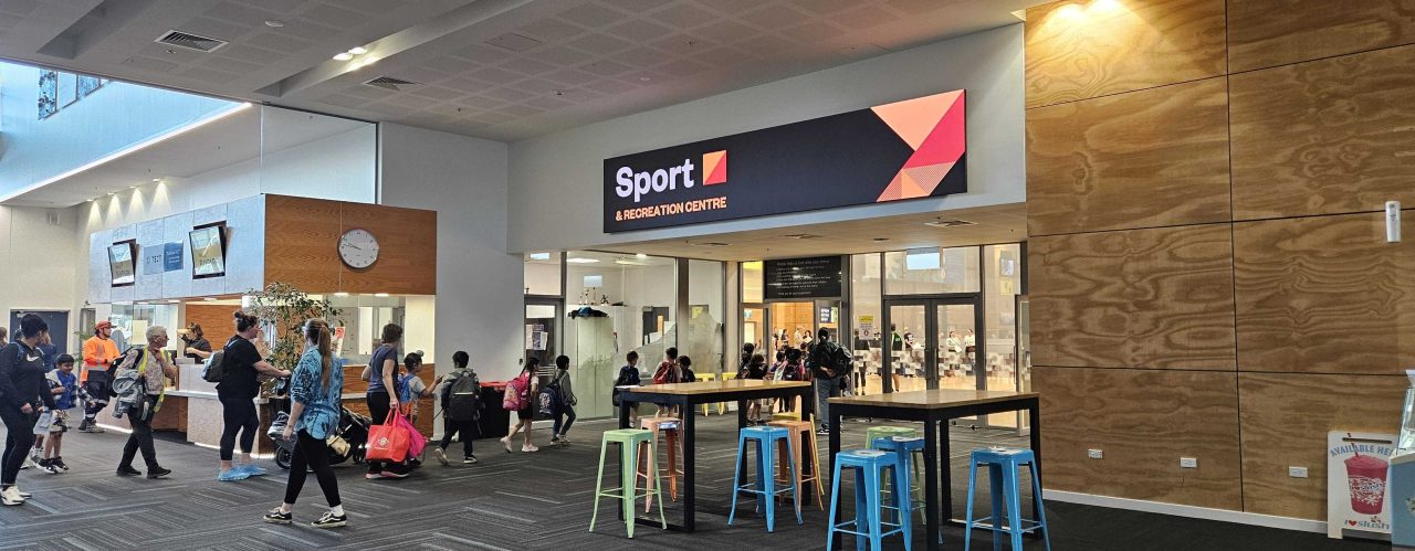 Visitors in the Baypark Arena foyer beneath a digital sign.