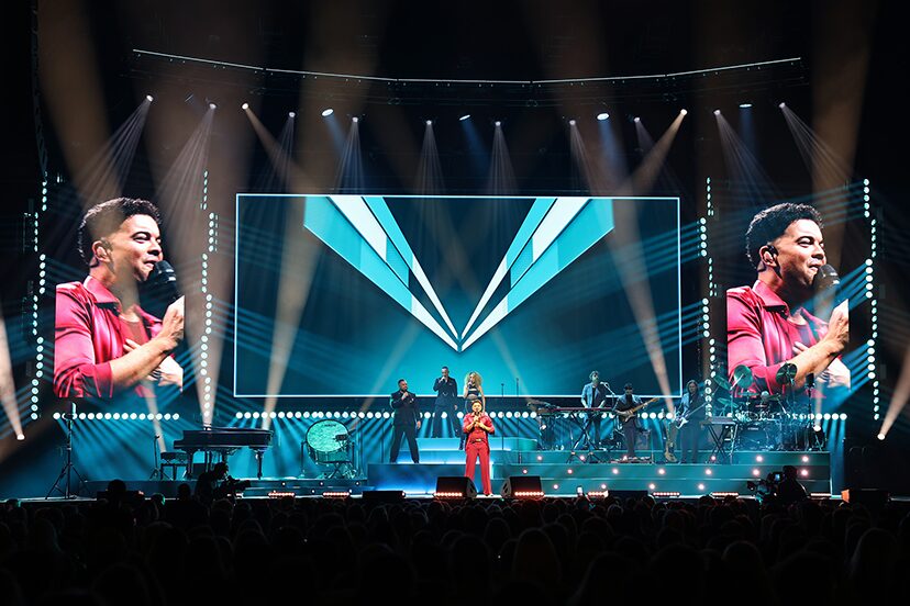 Geometric blue graphics across the stage screen between live video portraits on the tour.