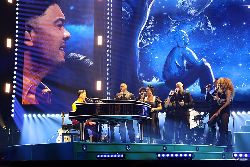 Piano and band on stage beneath blue video screens during the 100 Times Around the Sun tour.