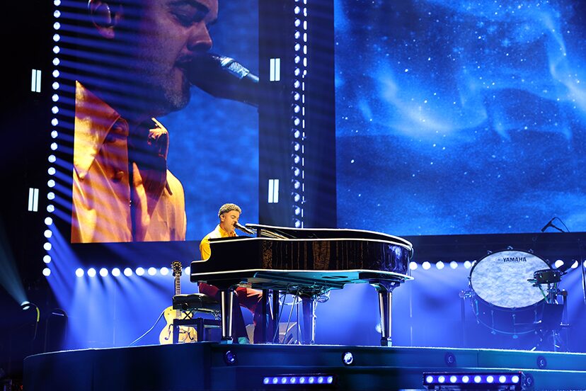 Piano performance against a blue video backdrop on the 100 Times Around the Sun tour.