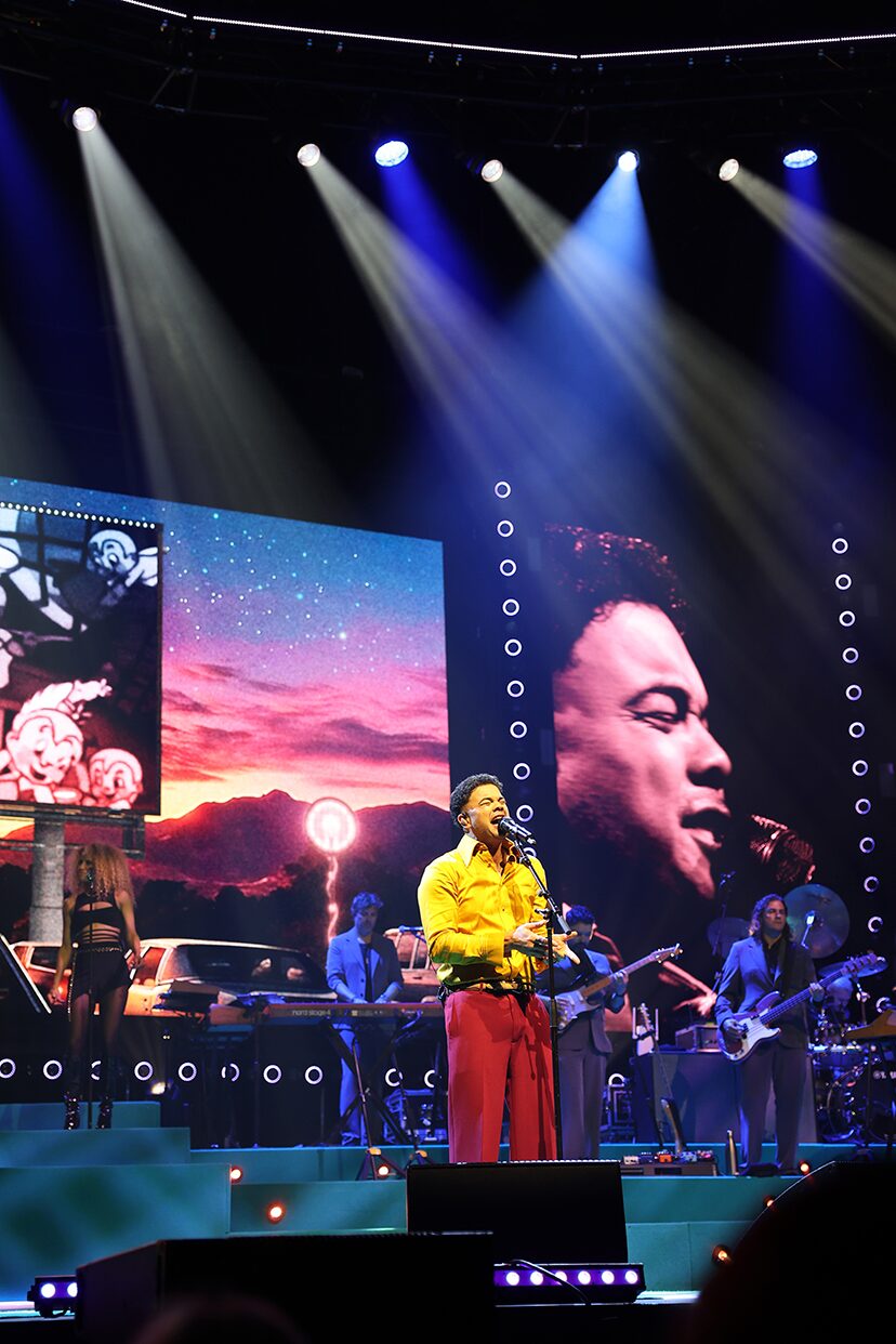 Performer and live video portrait beneath blue beams on the 100 Times Around the Sun tour.