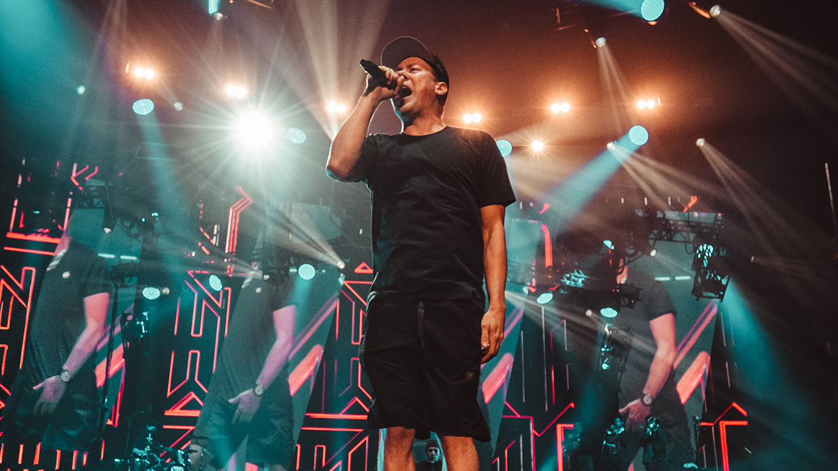 Vocalist performs in front of patterned video panels and bright stage lights at the Hilltop Hoods show.