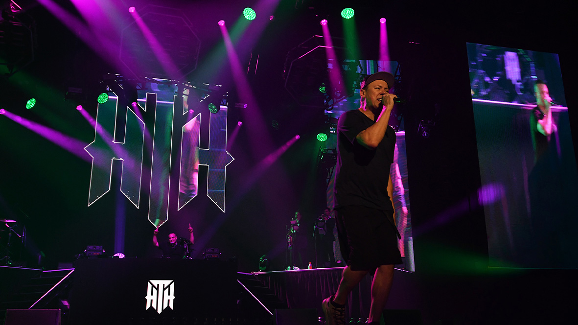 Purple and green lighting around the Hilltop Hoods emblem behind a performer.