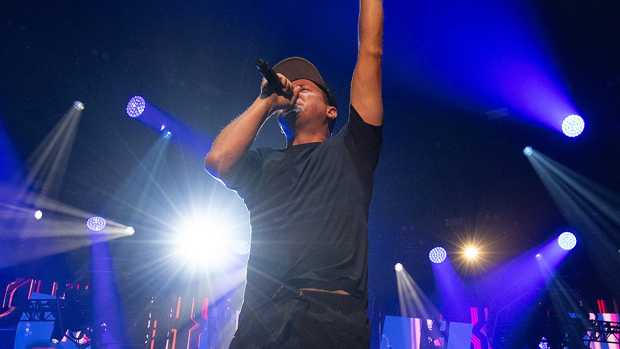 Vocalist raises an arm beneath blue and white stage beams at the Hilltop Hoods show.