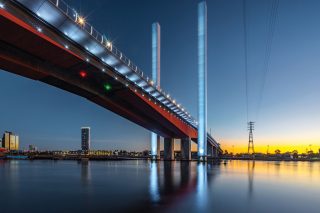 Illuminated towers of Melbourne’s Bolte Bridge reflected in the water at sunset.
