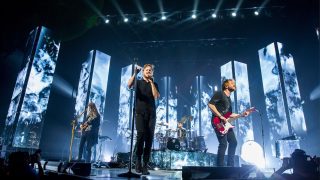 Imagine Dragons performing between tall blue and white video panels.
