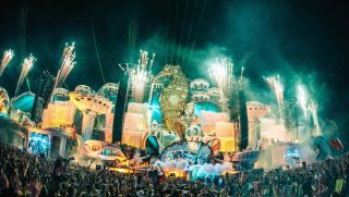 Green lasers and pyrotechnics above an elaborate Tomorrowland festival stage and a packed crowd.